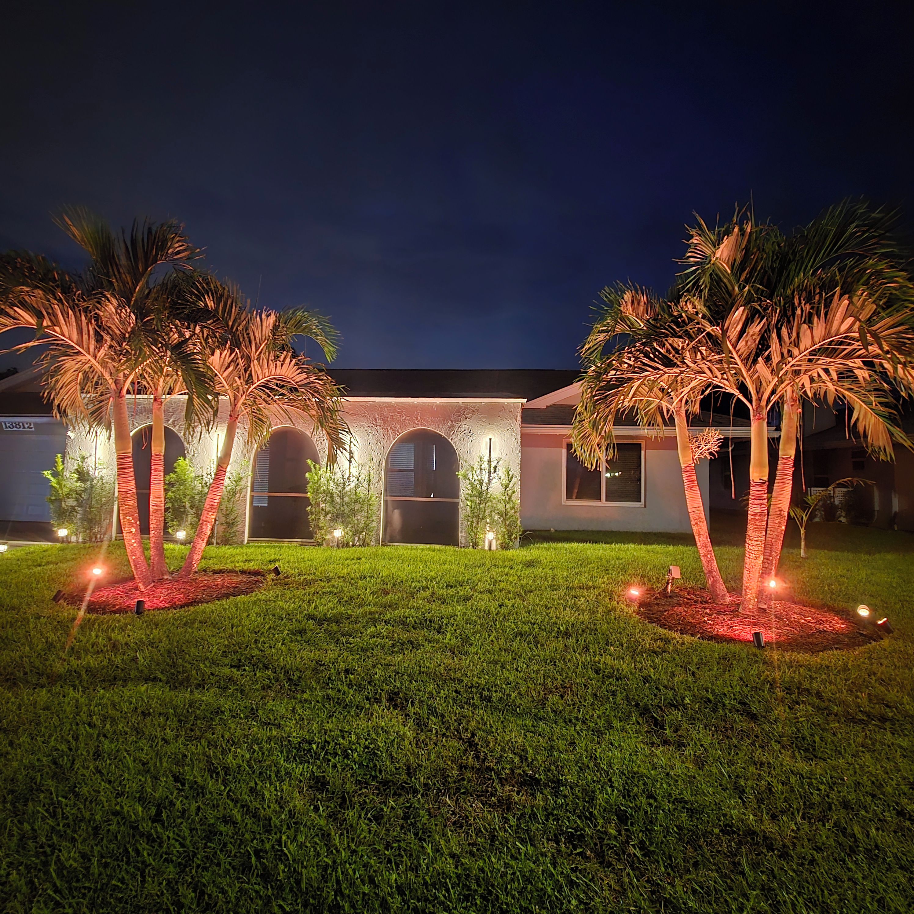 A building with a symmetrical facade, arched windows, and a well-maintained lawn with palm trees.