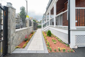 A pathway flanked by a stone wall and a white fence, leading to a building with a wooden facade and a white balcony.