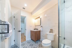 Een moderne badkamer met een houten wastafelmeubel, een toilet en een douchecabine met glazen wanden.