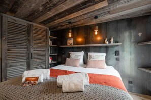 A bedroom with a large bed, wooden slatted wardrobe, and built-in shelving with books and decorative items. - Le Refuge du Bez - Pistes de ski à 100m (La Salle-les-Alpes)