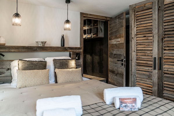 Quarto com cama, almofadas, mesa de cabeceira, abajur, guarda-roupa e luminária suspensa.