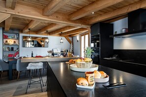 A modern kitchen with a central island, bar stools, and a dining area with a view of the living room.