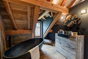 A rustic bathroom with a freestanding bathtub, wooden beams, and a dark wall with circular mirrors.