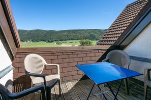 A balcony with a view of a green landscape and a house. There are two chairs and a table. - La Moucherolle - Station de ski accessible à pied (Méaudre)