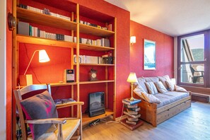 A cozy room with a wooden bookshelf, a comfortable sofa, a television, and a window with a view. - La Moucherolle - Station de ski accessible à pied (Méaudre)