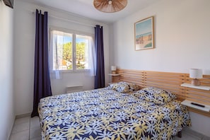 A bedroom with a bed, a window with curtains, a painting on the wall, and a bedside table with a lamp. - La Maison de Canet - 100m de la plage (Canet-en-Roussillon)