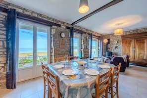 A dining area with a table set for four, stone walls, and a view of the sea. - Villa Les Mouettes - Face à la baie (Saint-Michel-en-Grève)