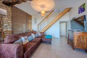 Een woonkamer met een bruine leren bank, een houten tv-meubel, een trap en een stenen muur.