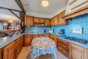 A kitchen with wooden cabinets, a gas stove, a sink, and a blue tiled backsplash. - Villa Les Mouettes - Face à la baie (Saint-Michel-en-Grève)