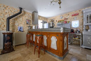 A kitchen with a stone wall, a central island with stools, a vintage stove, and a clock on the wall. - Le Coin Rétro - Proche d'Avignon (Le Thor)