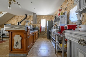 A kitchen with stone walls, a wooden bar, and a variety of appliances. - Le Coin Rétro - Proche d'Avignon (Le Thor)