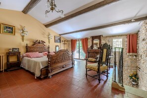 A bedroom with a wooden bed, a stone wall, and a chandelier. - Le Coin Rétro - Proche d'Avignon (Le Thor)