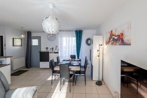 Ein moderner Essbereich mit Tisch für vier Personen, eine Küche im Hintergrund und eine Wohnbereich mit Sofa und Lampe.