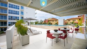 A rooftop patio with outdoor seating, a swimming pool, and a view of surrounding buildings. - Jacana Serenity 206 | Bucerias Beach & Rooftop Infinity Pool (Nuevo Vallarta)