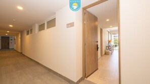 A hotel corridor with a wooden door, a number sign, and a view into a room with a table and chairs. - Jacana Serenity 206 | Bucerias Beach & Rooftop Infinity Pool (Nuevo Vallarta)