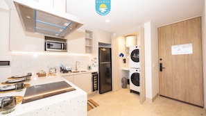 A modern kitchen with a microwave, refrigerator, and washing machines. - Jacana Serenity 206 | Bucerias Beach & Rooftop Infinity Pool (Nuevo Vallarta)
