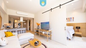 A modern living room with a sofa, coffee table, TV, and a kitchen area with a microwave and oven. - Jacana Serenity 206 | Bucerias Beach & Rooftop Infinity Pool (Nuevo Vallarta)