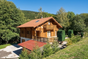 A wooden chalet with a red-tiled roof, a balcony, and a view of a forested hillside. - Chalet Caribou - Pour 6 avec terrasse (Ventron)