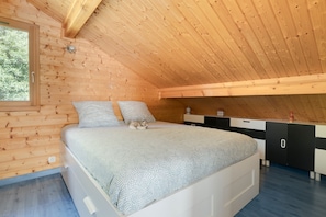 A bedroom with a wooden ceiling, a bed with patterned bedding, a dresser, and a window. - Chalet Caribou - Pour 6 avec terrasse (Ventron)