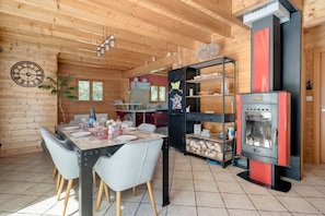 A wooden interior with a dining table set for four, a kitchen area with a stove, and a red refrigerator. - Chalet Caribou - Pour 6 avec terrasse (Ventron)