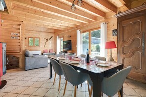 A wooden interior with a dining table set for four, a sofa, a television, and a fireplace. - Chalet Caribou - Pour 6 avec terrasse (Ventron)