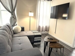 A modern living room with a sofa, a side table, a lamp, and a flat-screen TV mounted on the wall. - The hideaway of Limoilou, a cozy little urban nest (Québec)