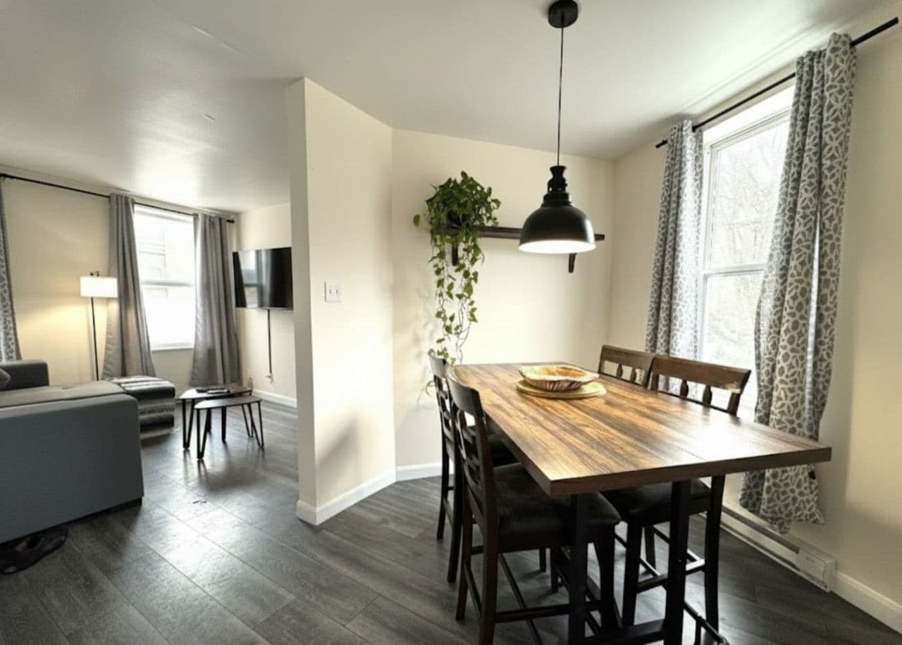 A modern dining area with a wooden table and chairs, a hanging plant, and a pendant light.