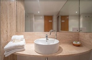 Ein Badezimmer mit einem runden Waschbecken, einem Spiegel, einem Stapel Handtüchern und einer kleinen Holzschale.