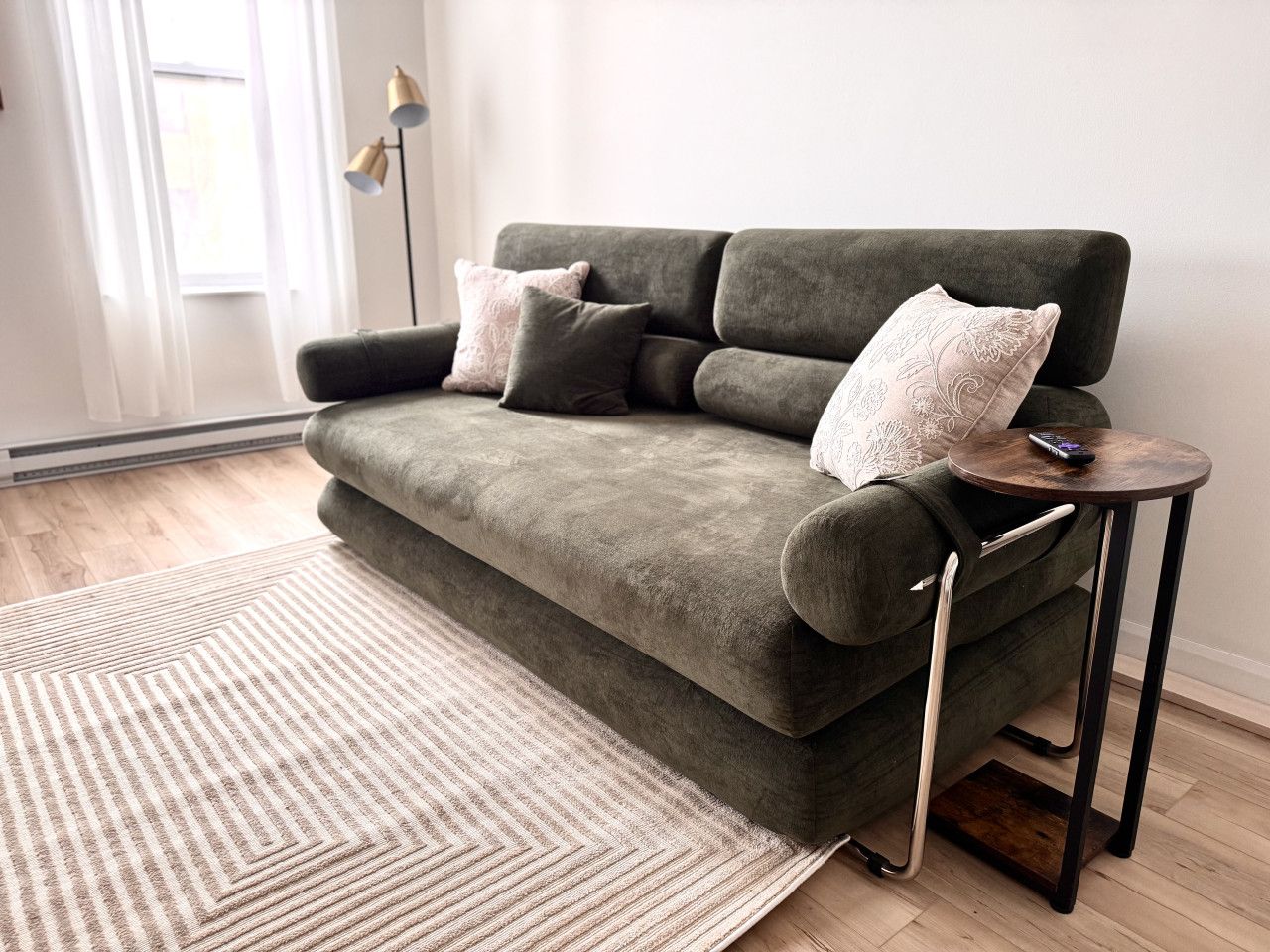 Ein modernes Wohnzimmer mit einem grauen Sofa, einem runden Holztisch und einem gestreiften Teppich.