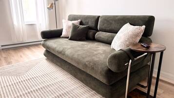 Ein modernes Wohnzimmer mit einem grauen Sofa, einem runden Holztisch und einem gestreiften Teppich.