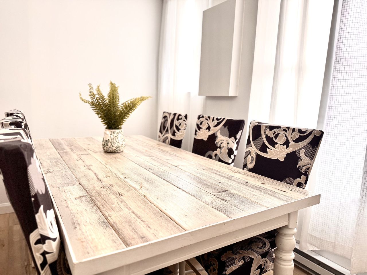 Ein Esstisch mit rustikaler Optik, umgeben von stuhlartigen Sitzgelegenheiten mit Stoffbezug und Muster.