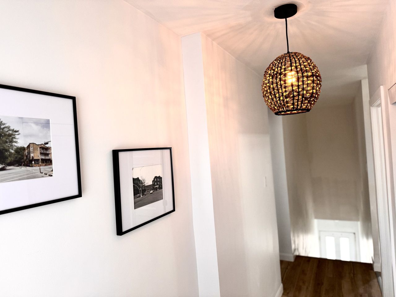Ein Flur mit zwei gerahmten Fotografien an der Wand, einer strukturierten Pendelleuchte und einer Tür am Ende.
