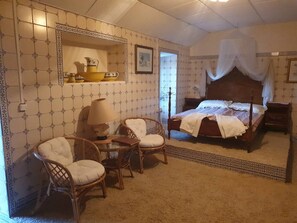 Ein Schlafzimmer mit einem Himmelbett, zwei Stühlen, einem Nachttisch und einem Spiegel.