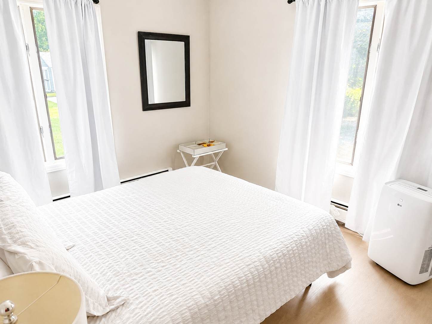 A bedroom with a bed, a bedside table, a mirror, and a window with curtains.