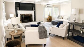 A modern living room with a fireplace, white sofas, a coffee table, and a TV.