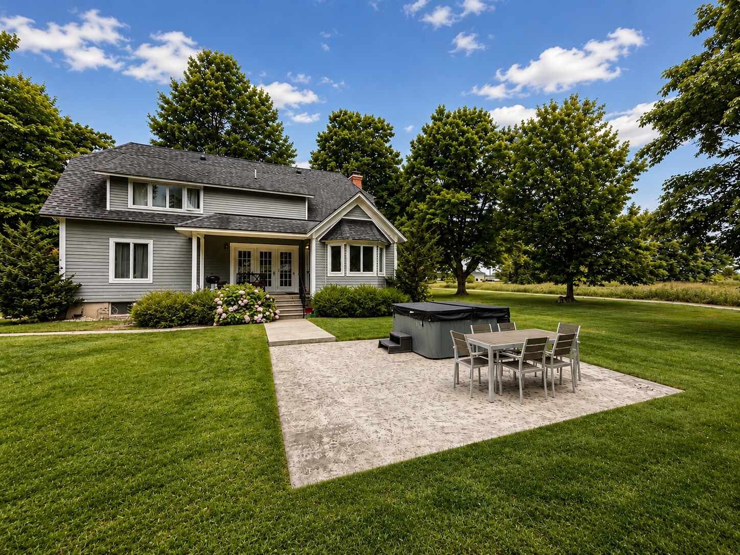 A two-story house with a patio area featuring a table and chairs, a hot tub, and a well-maintained lawn.