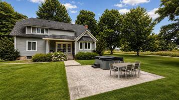 A two-story house with a patio area featuring a table and chairs, a hot tub, and a well-maintained lawn.