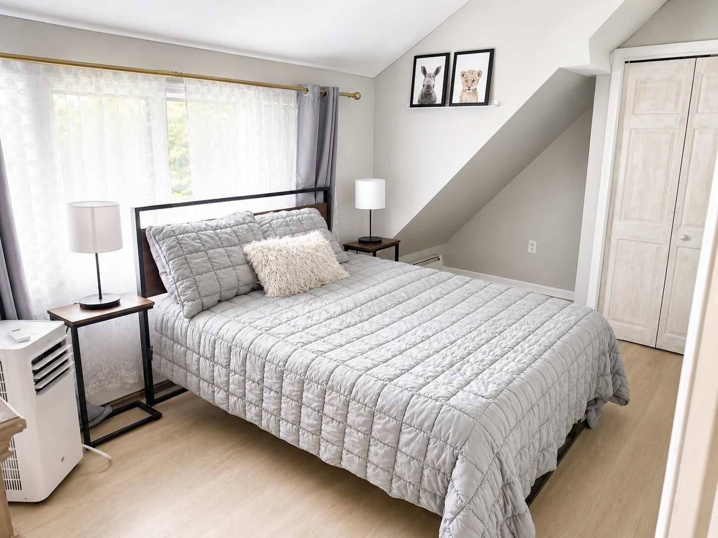 A bedroom with a bed, bedside tables, a lamp, a heater, a window with curtains, and a door.