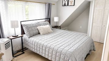 A bedroom with a bed, bedside tables, a lamp, a heater, a window with curtains, and a door.