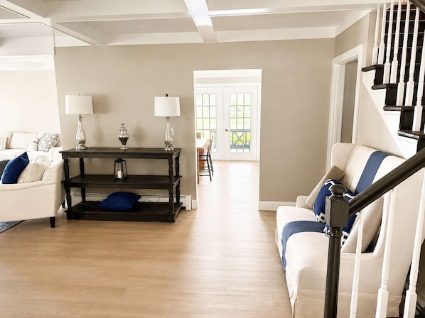 Una sala de estar con un sofá, una mesa con lámparas, una escalera y una vista a través de una puerta.