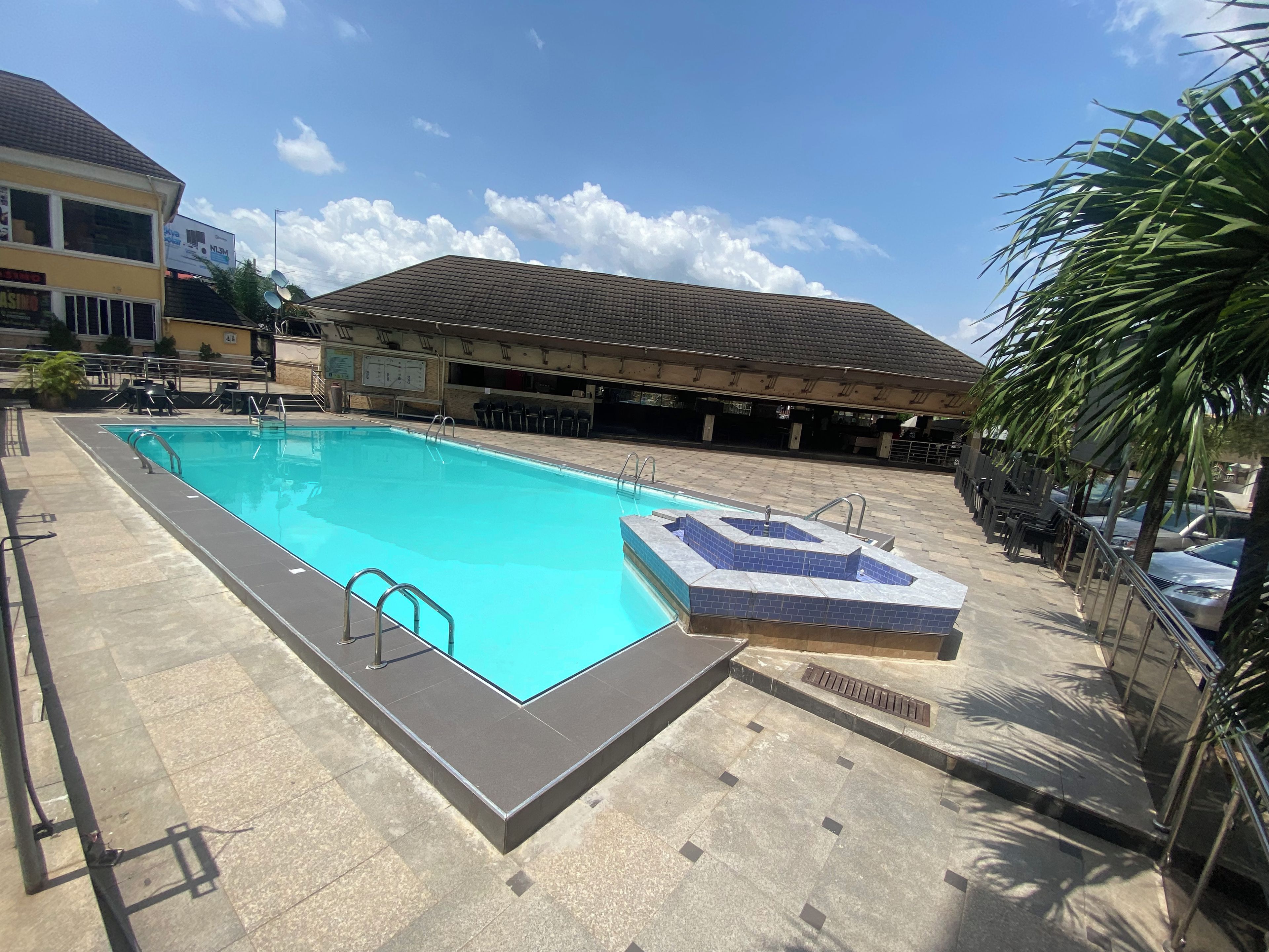 A swimming pool with a tiled deck, a lifeguard stand, and a covered seating area in the background.