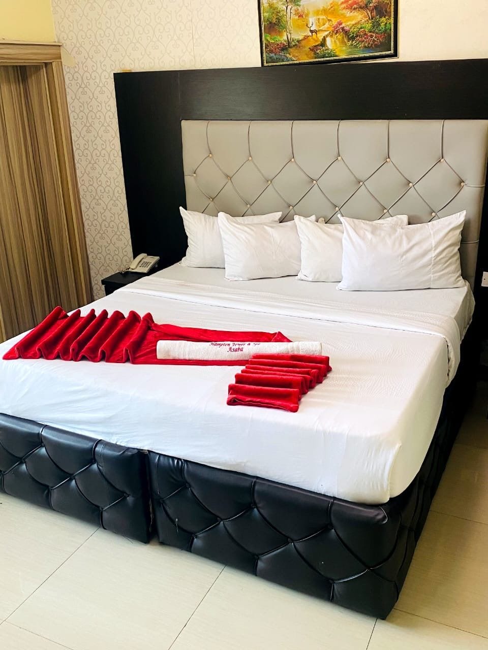 Een hotelkamer met een bed, wit beddengoed, een zwart hoofdeinde en een rode handdoekopstelling.