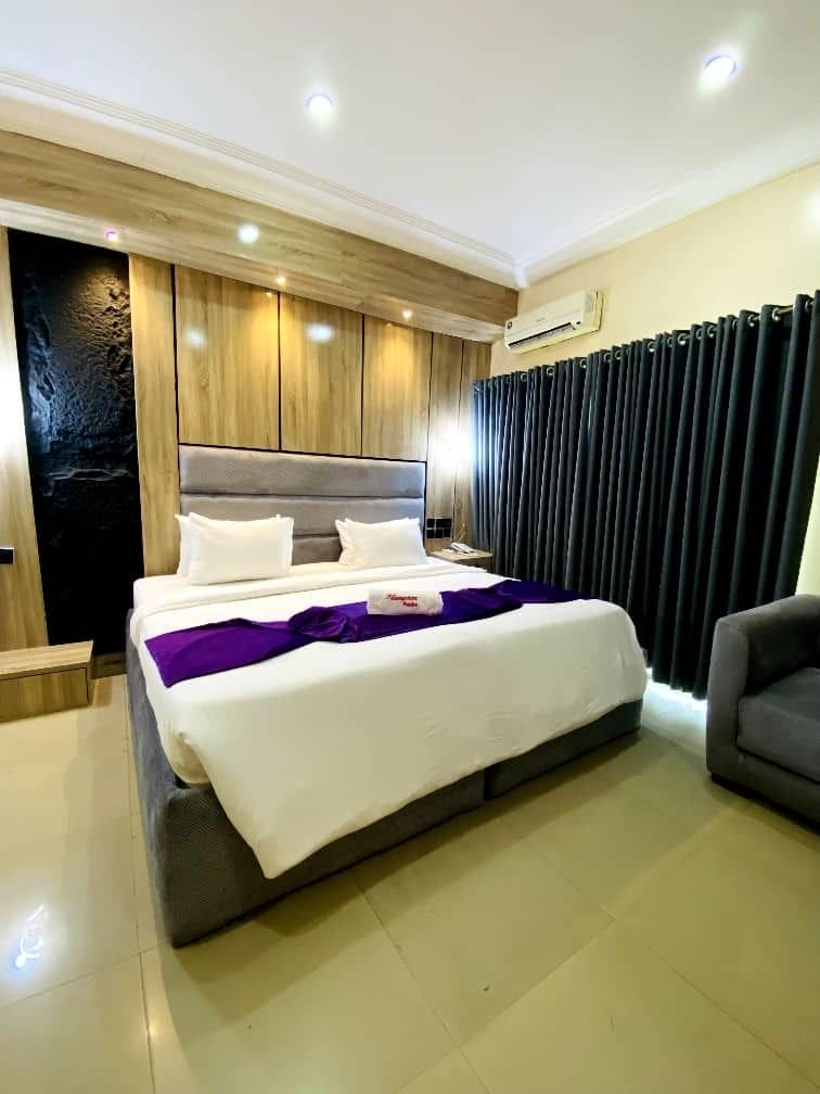 Una habitación de hotel moderna con una cama grande, una mesita de noche, una silla y aire acondicionado integrado.