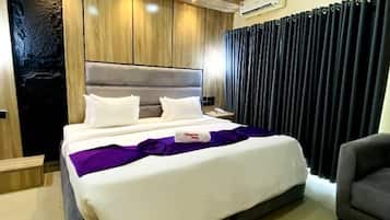 Una habitación de hotel moderna con una cama grande, una mesita de noche, una silla y aire acondicionado integrado.
