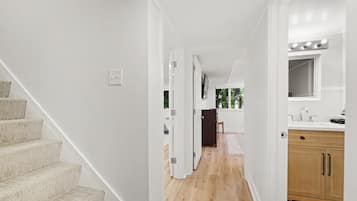 Un intérieur moderne comprenant un escalier, un coin cuisine et un couloir menant à une chambre.