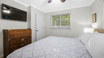 A bedroom with a bed, a dresser, a television, a window with blinds, and a ceiling fan.