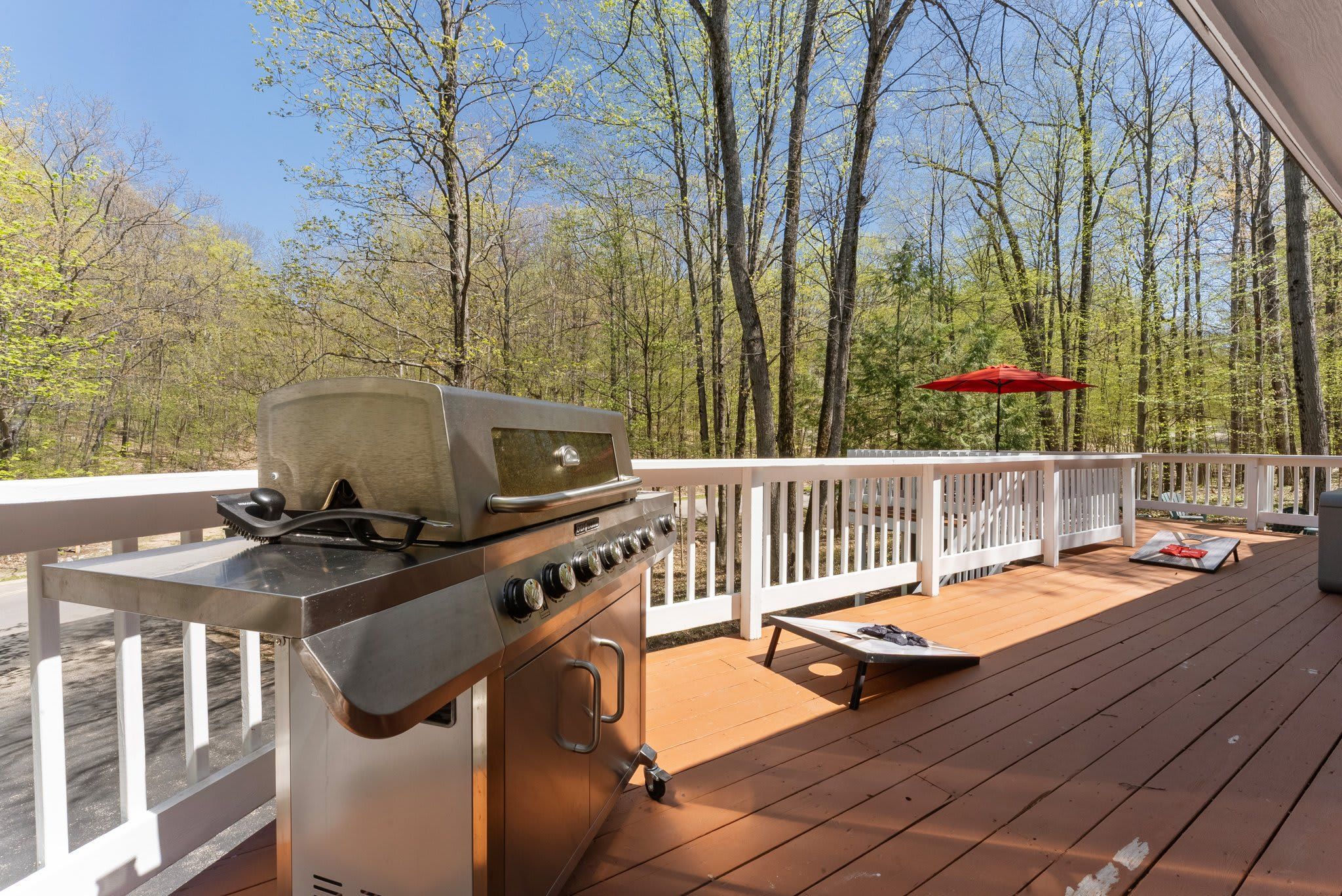 A deck with a stainless steel grill, a red umbrella, and a white railing.