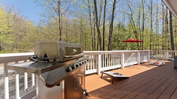 A deck with a stainless steel grill, a red umbrella, and a white railing.