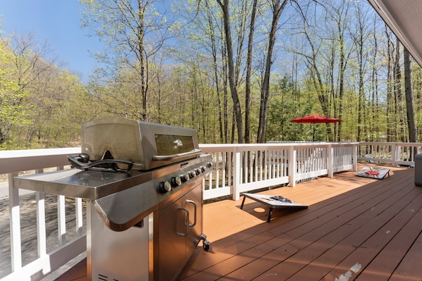A deck with a stainless steel grill, a red umbrella, and a white railing.
