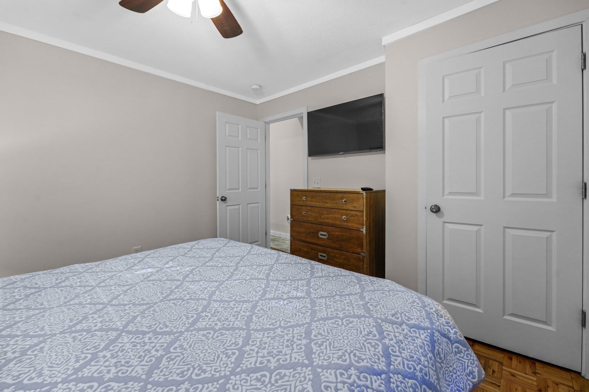 A bedroom with a bed, a dresser, a television on the wall, and two doors.